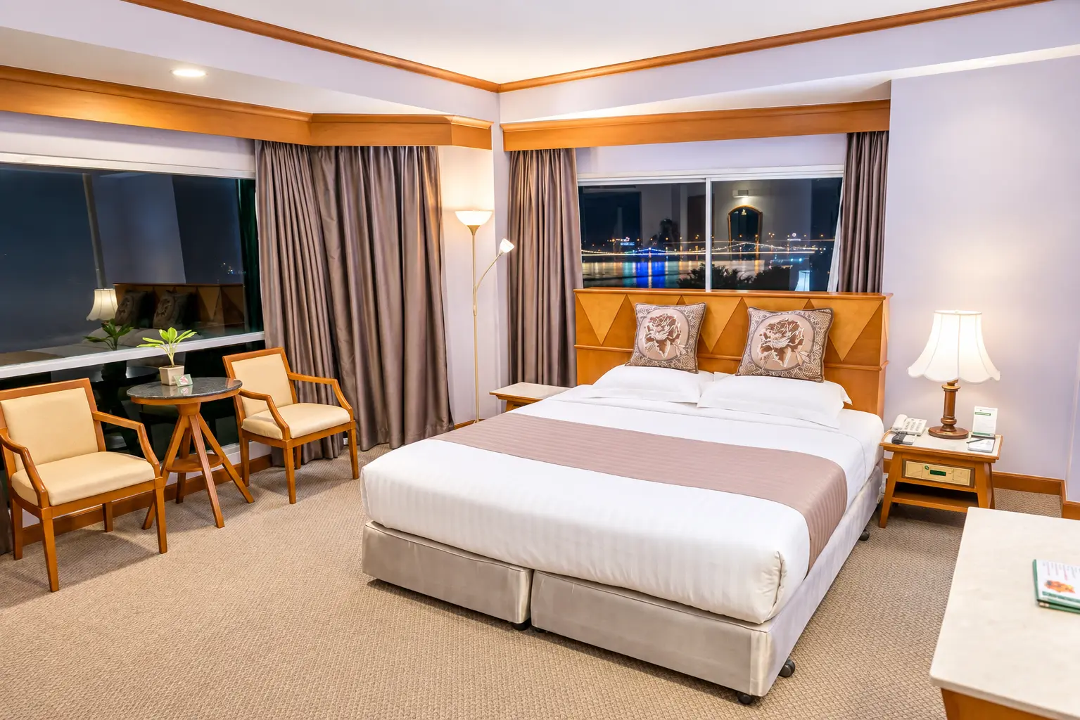 A hotel room at The Viang Tak Riverside, with the lit-up bridge visible through the window at night