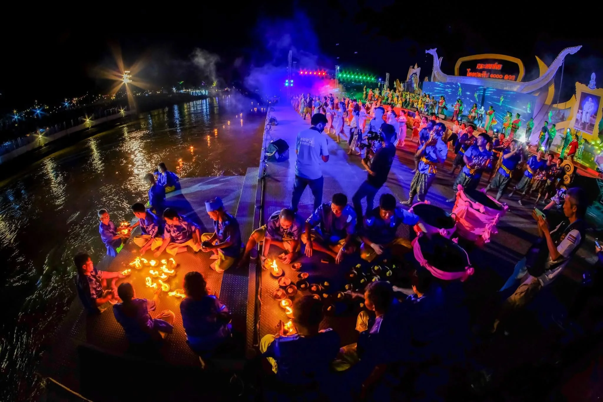 A person releasing a lit coconut-shell krathong into the river at night