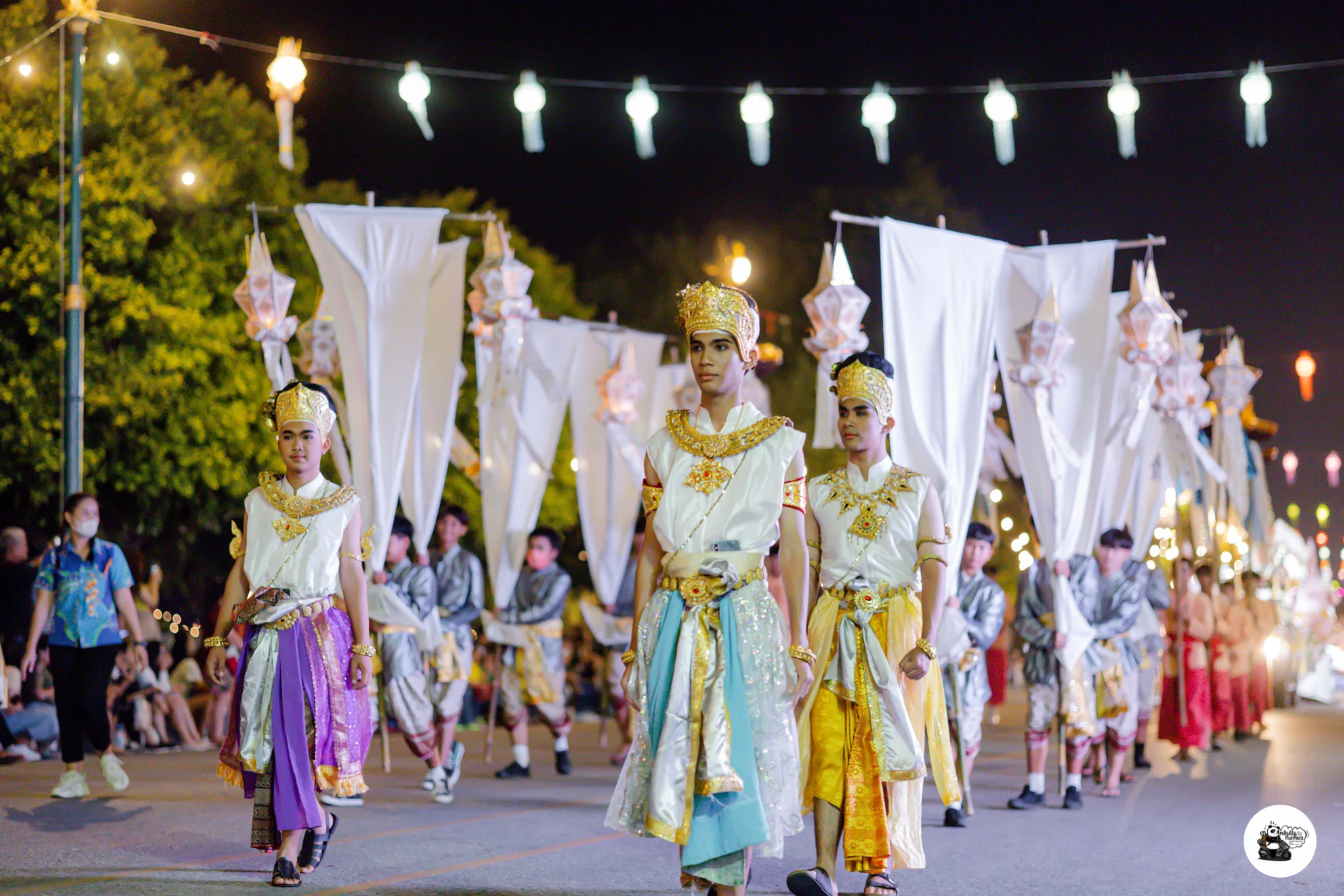 Young lantern bearers in white and gold traditional dress leading the procession, tall lantern staffs overhead
