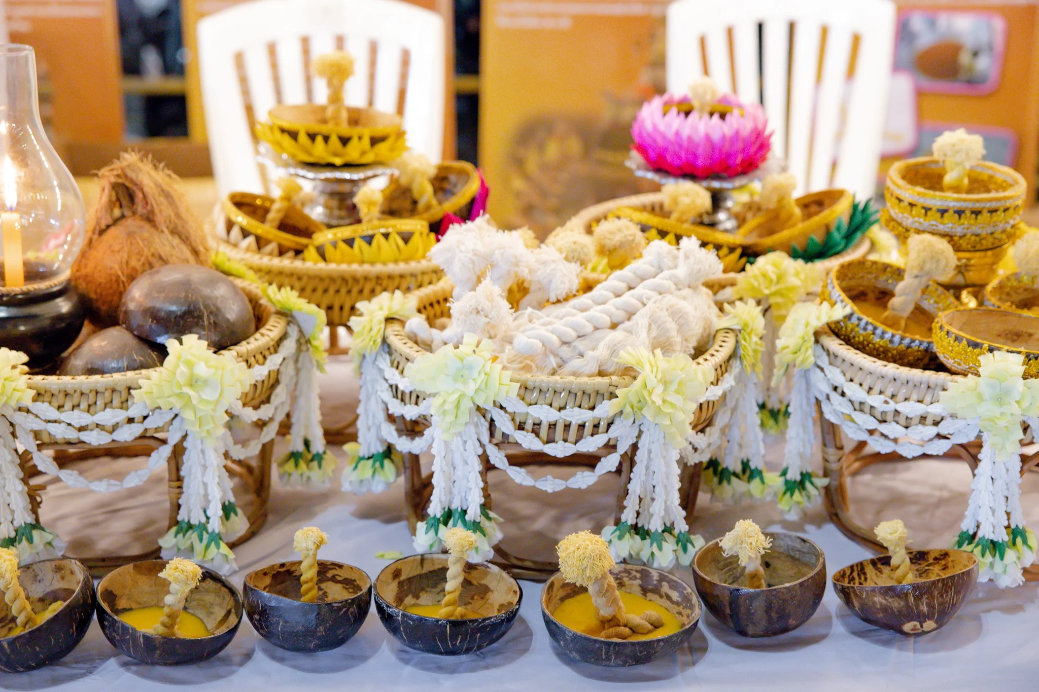 Whole coconuts, empty shells, and finished krathong sai laid out together on a craft table, showing every stage from raw material to finished offering