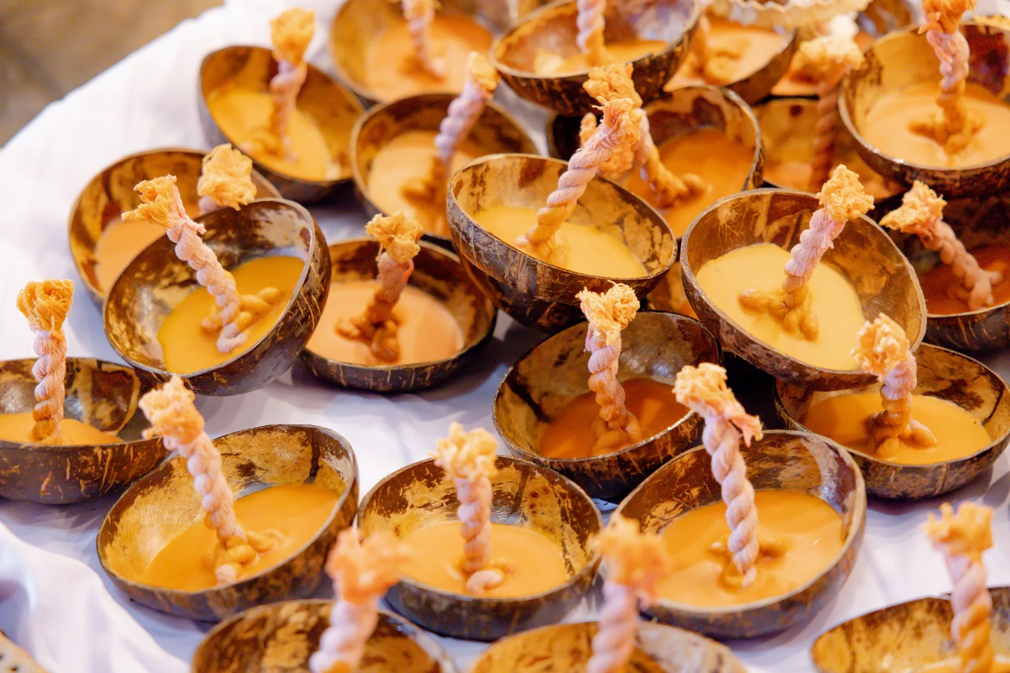 Dozens of coconut-shell candles, each filled with wax and a twisted cotton wick, laid out in rows